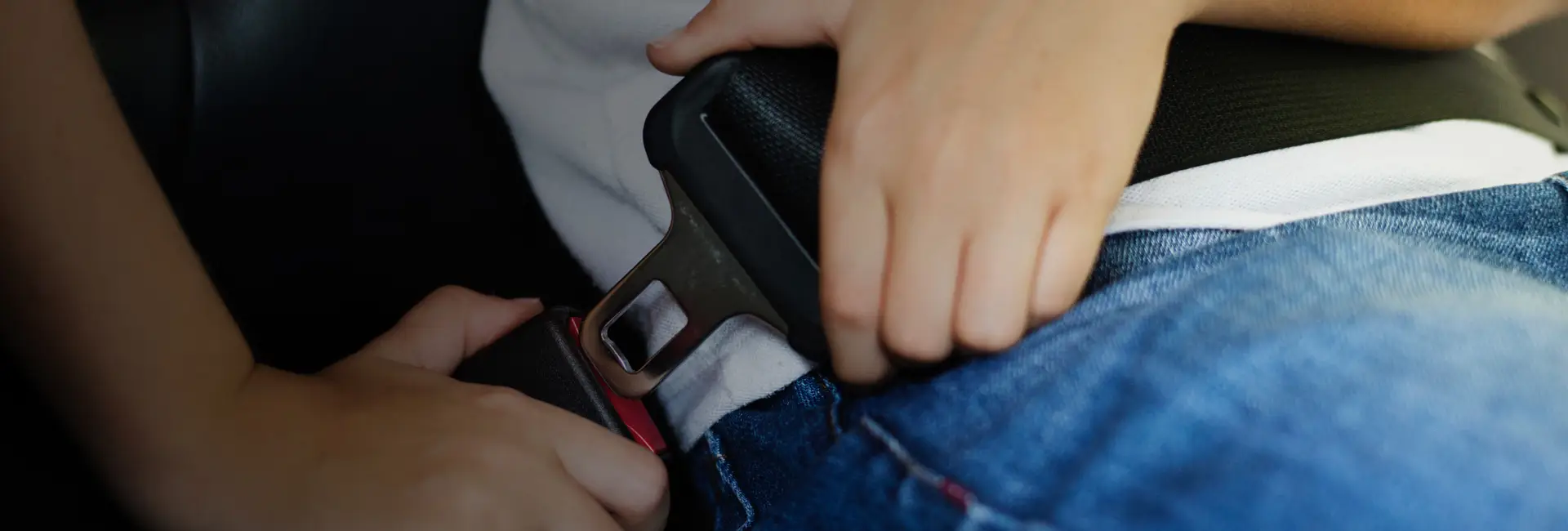 An adult fastening a child’s seatbelt in a car